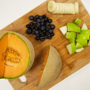 Cutting board with cantaloupe, blueberries, apple and bananas 