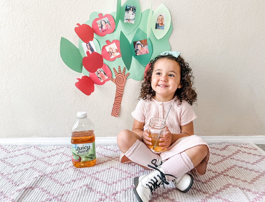 Little girl sitting with her family tree drinking Juice Jice 100% Apple juice