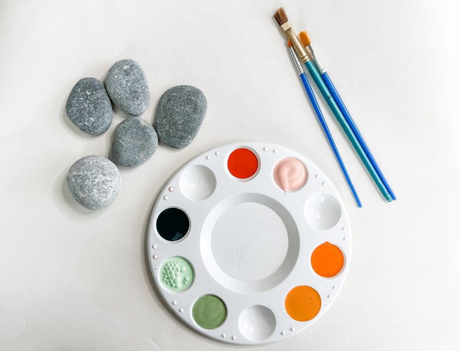 All of the positivity rock activity supplies. Including small smooth rocks, paints on the palette, assorment of brushes, and some scrap paper