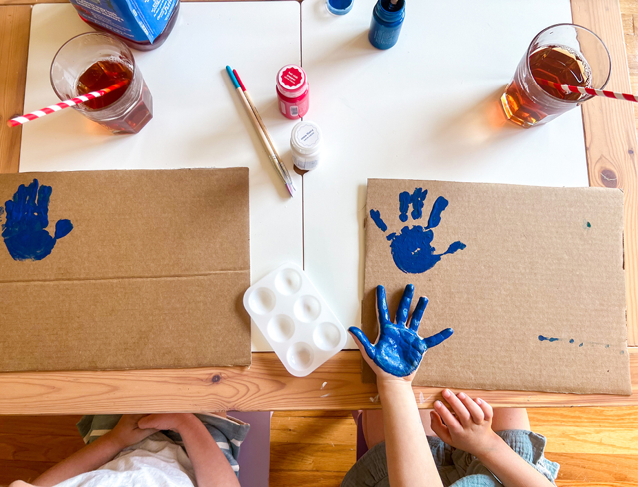 Young children making handprints with blue paint on the cardboard, drinking juicy juice 100% juice