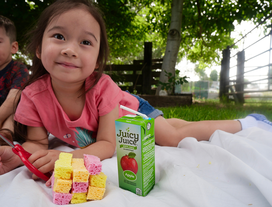 Young child smiling with her cut up sponged building the craft and sipping juicy juice
