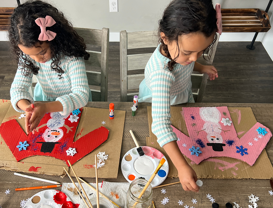 young children painting their cardboard cutout sweaters and adding designs with the supplies. Such as glitter and snowflakes